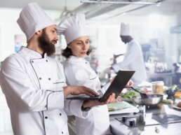 Zwei Köche planen die Warenwirtschaft mit dem Necta Group System. Sie optimieren Bestellprozesse in einer großen Edelstahl-Profi-Restaurantküche.