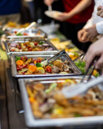 Buffet mit einer Auswahl an frischen Salaten und Hauptgerichten bei einer lebhaften Veranstaltung.