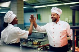 Glückliche Profiköche, die High-Five geben, während sie in der Restaurantküche arbeiten