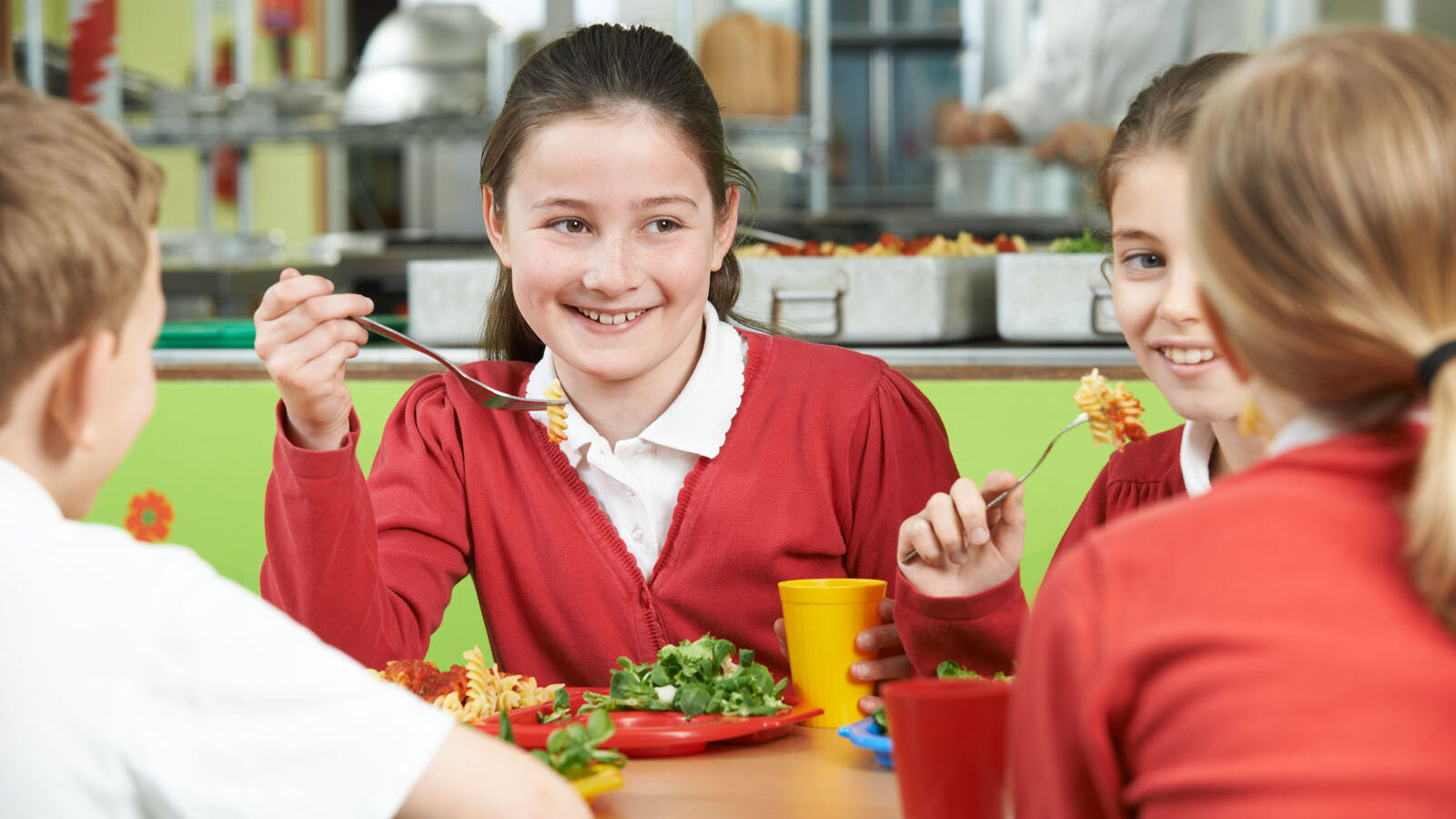 Schulkinder in roter Uniform beim gesunden Mittagessen in moderner Schulkantine